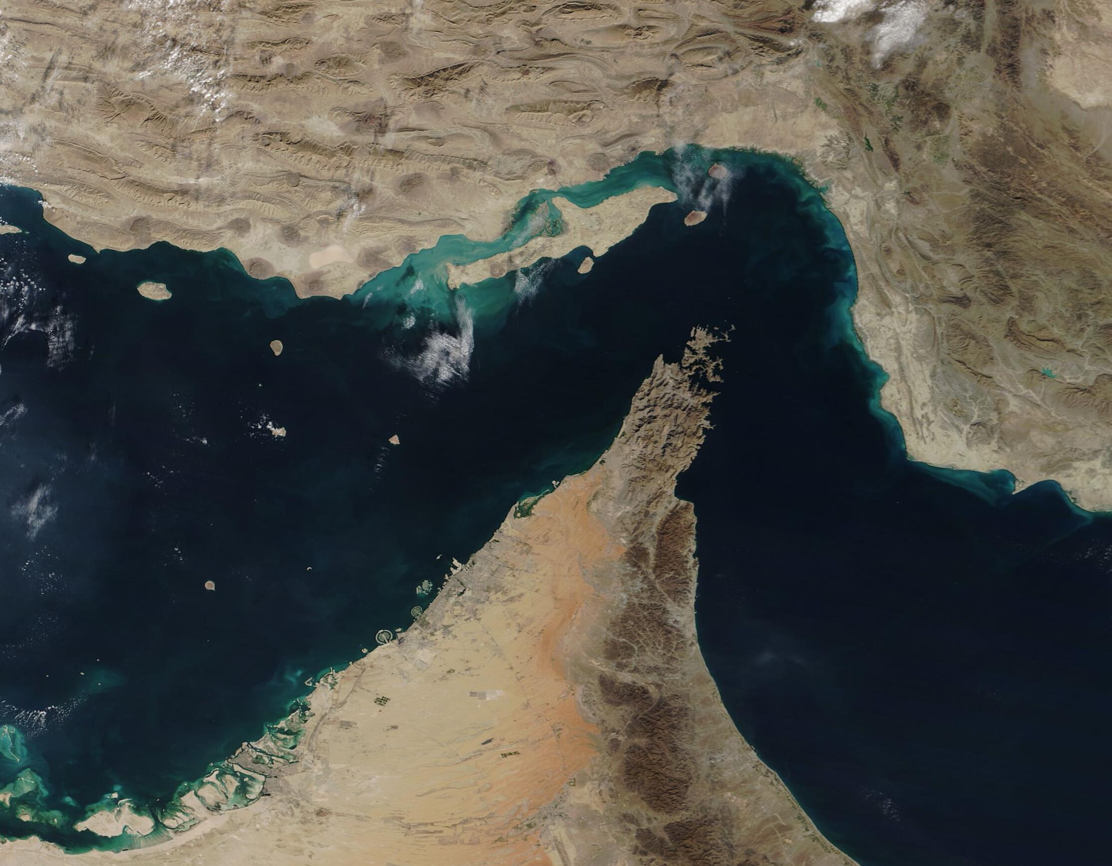 NASA satellite image of the Strait of Hormuz — the real waterway the game board is sampled from — with the Persian Gulf, the Iranian coast to the north, the Musandam Peninsula to the south, and the Gulf of Oman opening to the southeast.